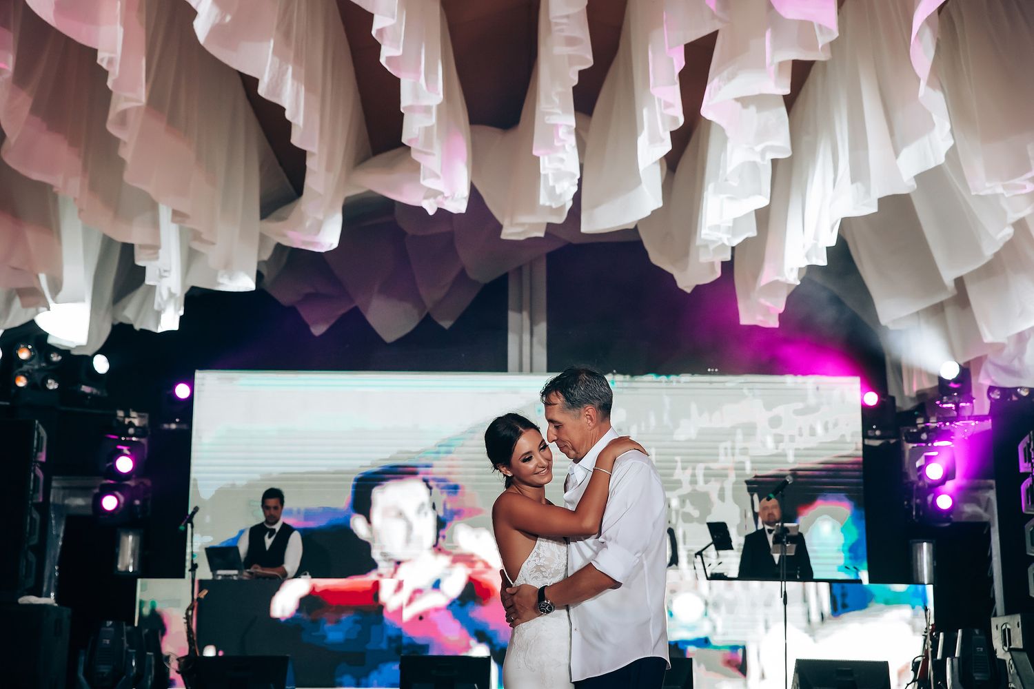 Wedding reception dance party with dramatic white ceiling draping and purple lighting.