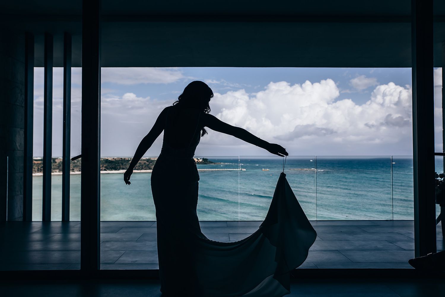A silhouette of a flowing dress against an ocean view through large windows.