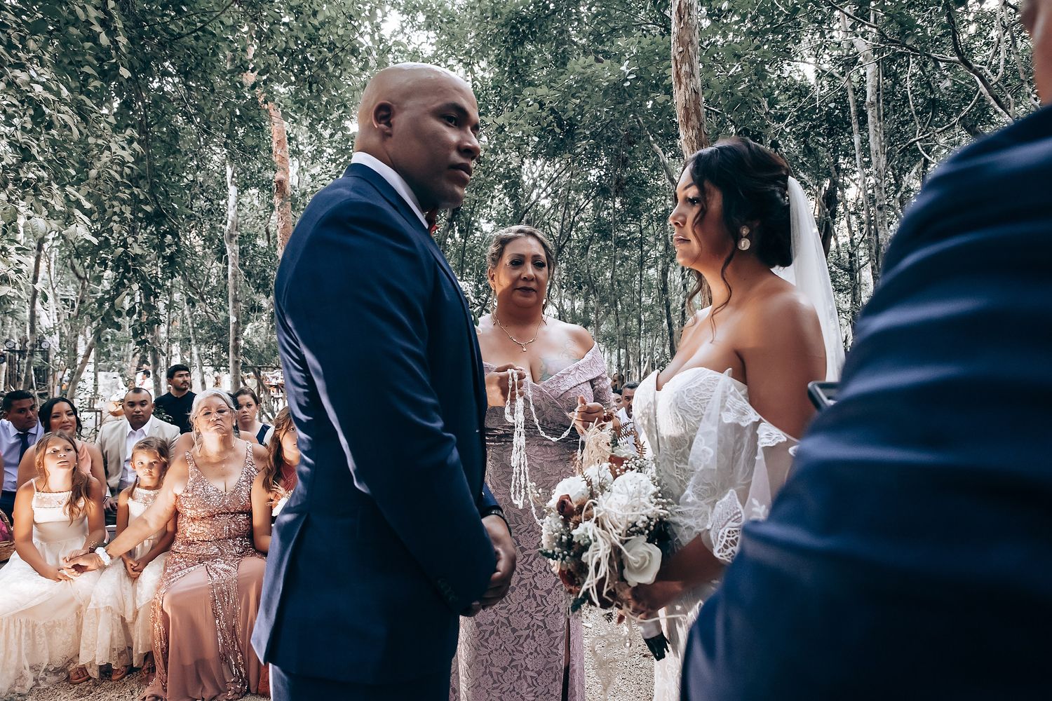 An emotional wedding ceremony exchange taking place in a forest surrounded by seated guests.