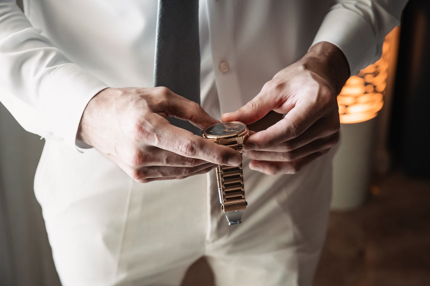 Groom in white suit fastening a gold watch on his wrist before wedding ceremony.