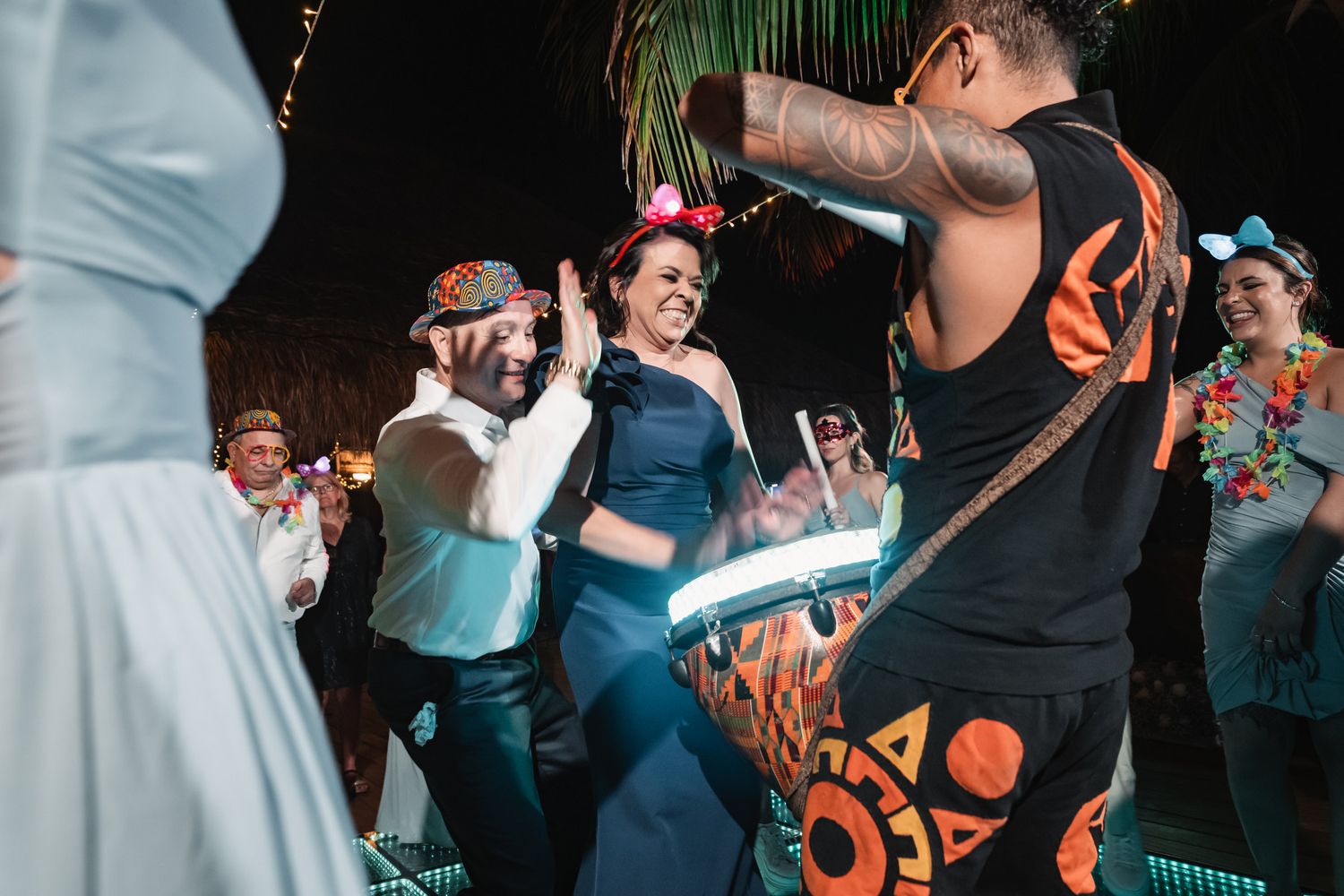 Wedding guests dancing energetically with live drummer performer at lively tropical beach reception party.