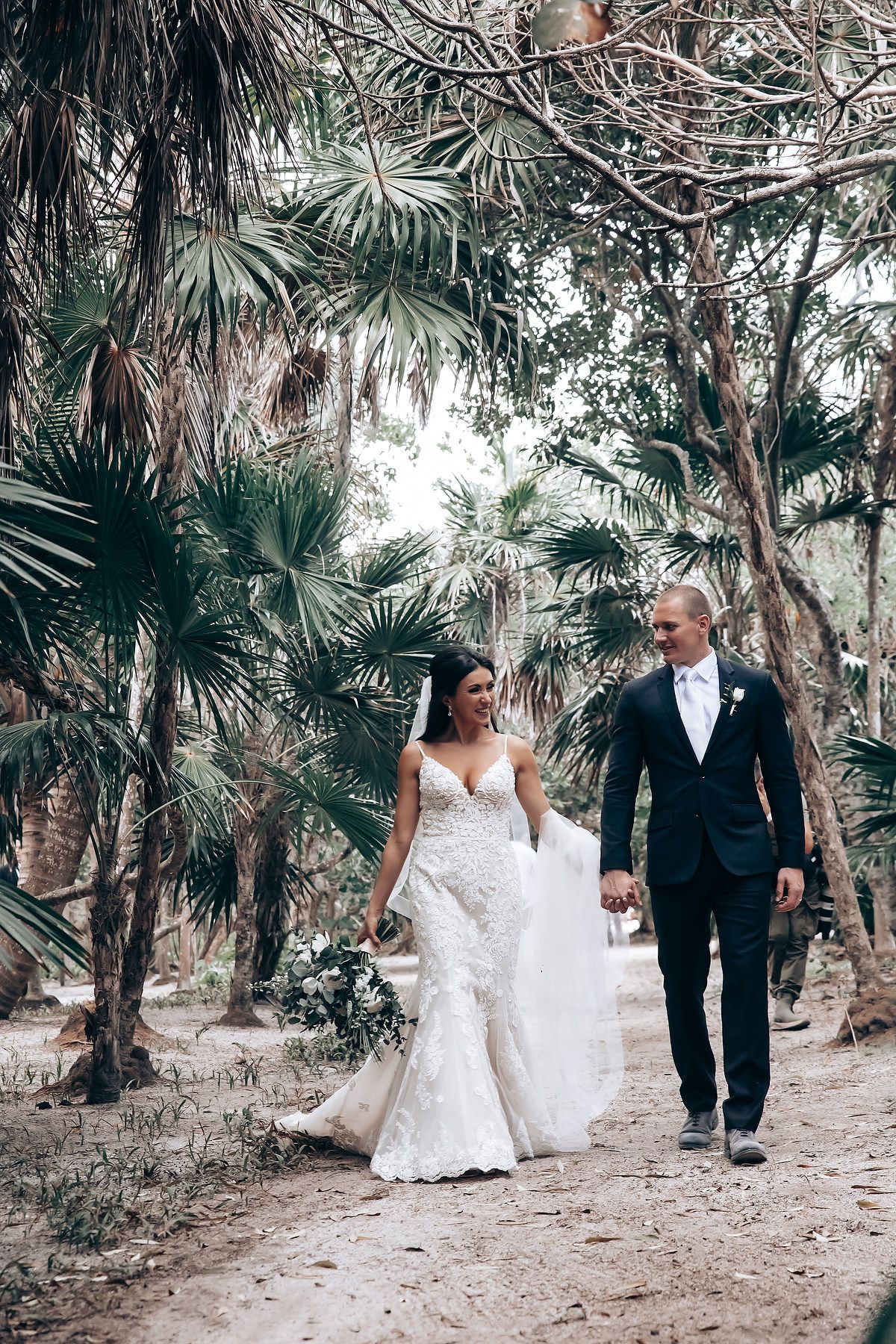 Wedding party walking through a palm tree lined path in formal attire.