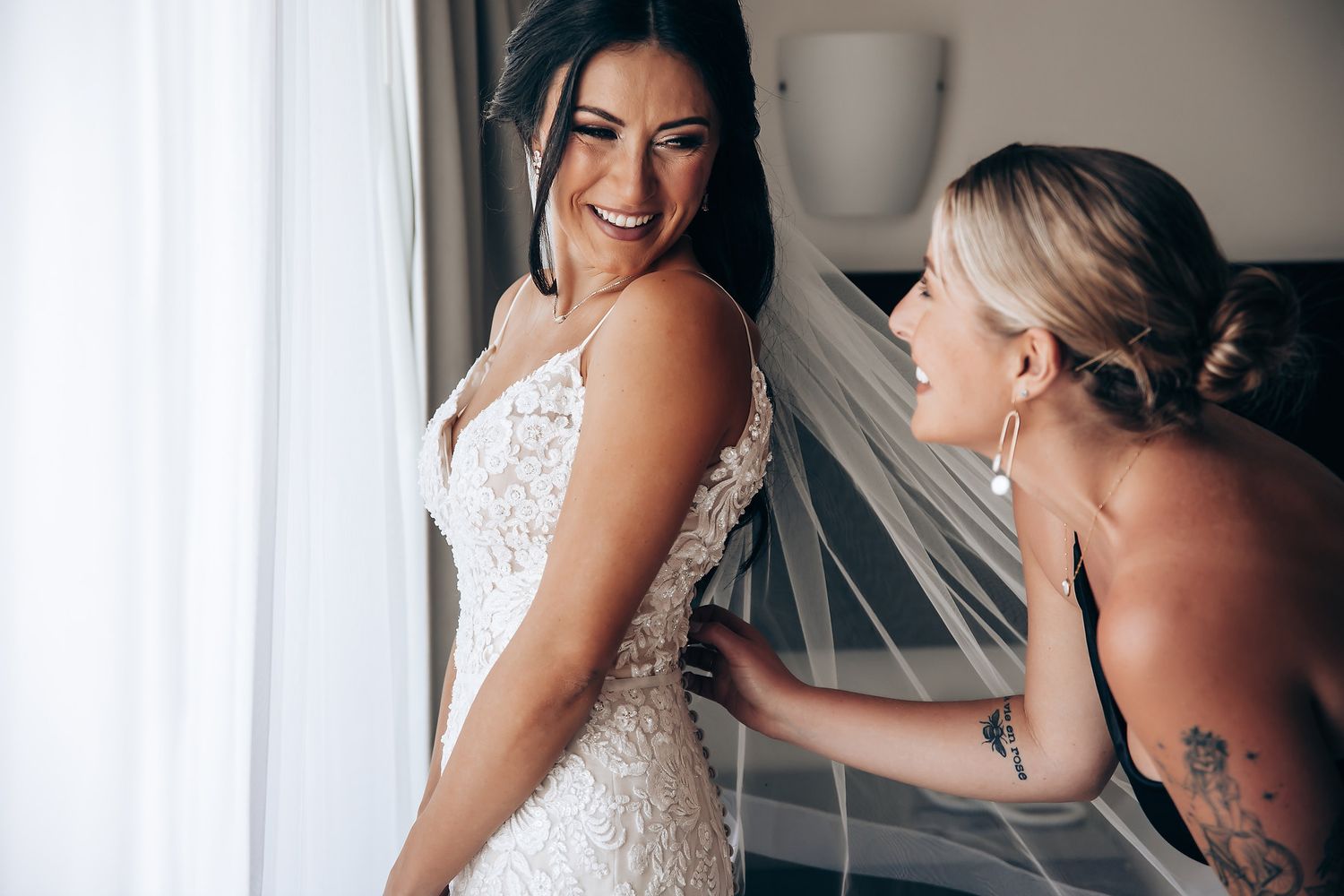 Two people share a joyful moment while adjusting a wedding dress and veil.