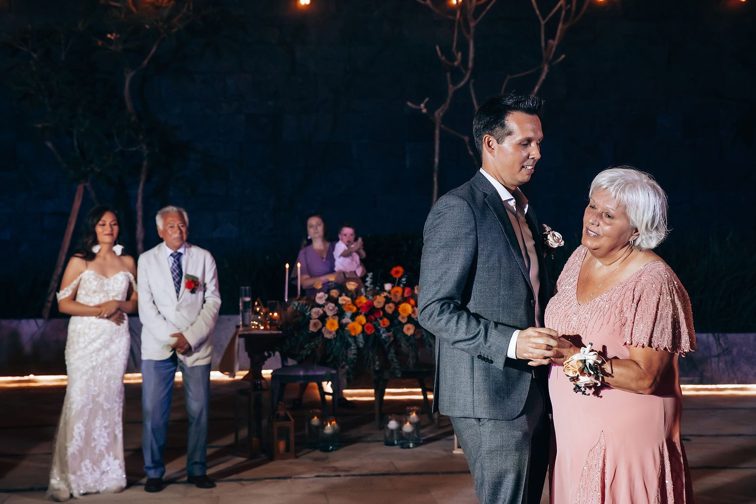 A couple shares a romantic dance moment under soft lighting at their evening wedding celebration.