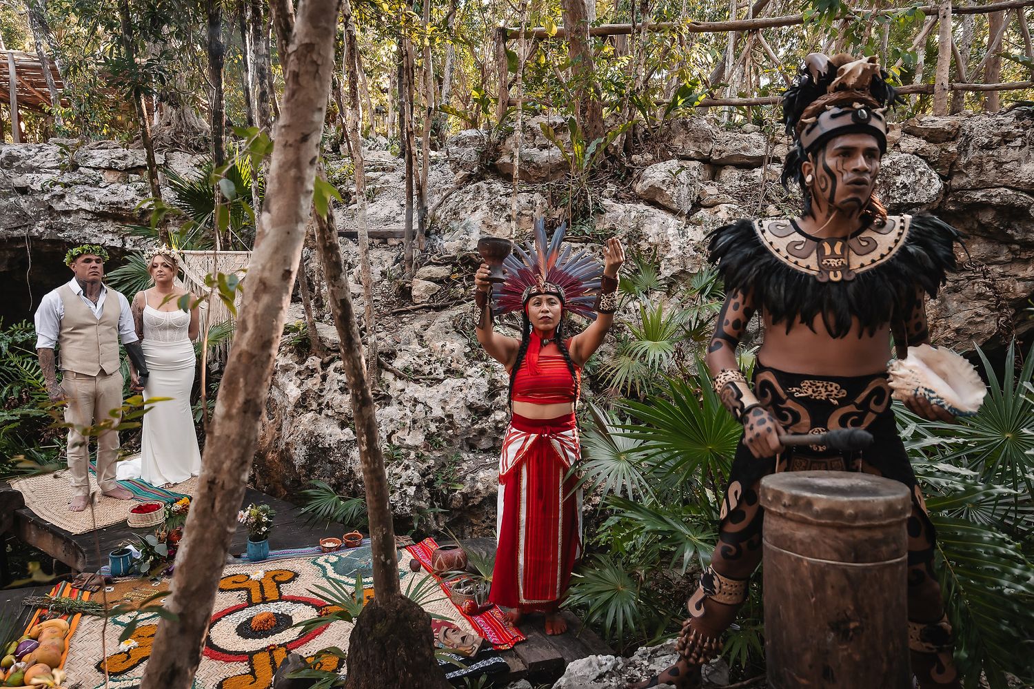 Mayan wedding ceremony in a lush jungle cenote with costumed performers in traditional attire alongside a bride and groom.