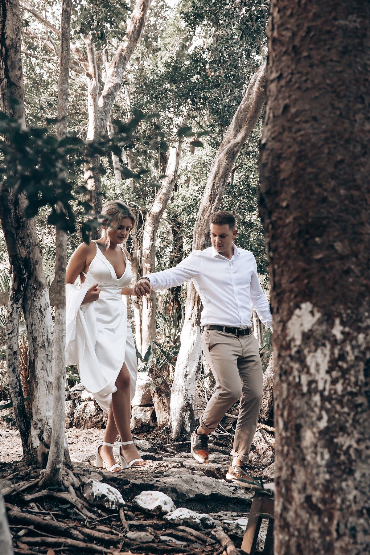 A couple walks together through a wooded area with tall trees on a sunny day.