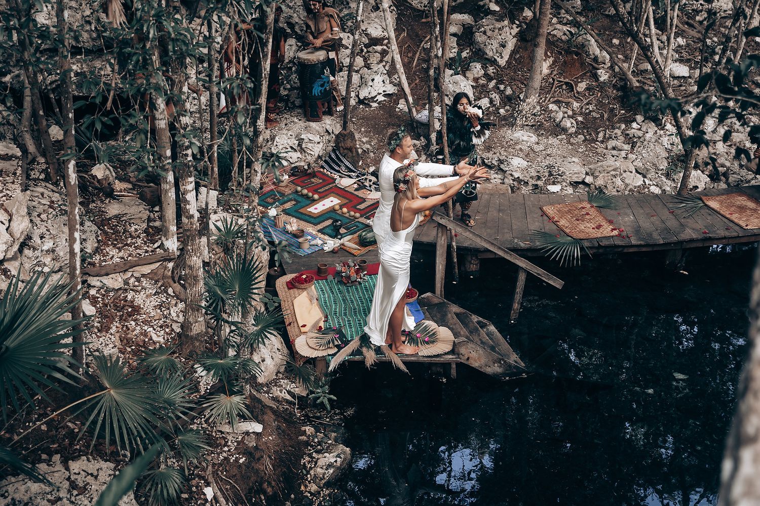 Wedding ceremony setup in a natural cave with wooden platforms and tropical greenery.