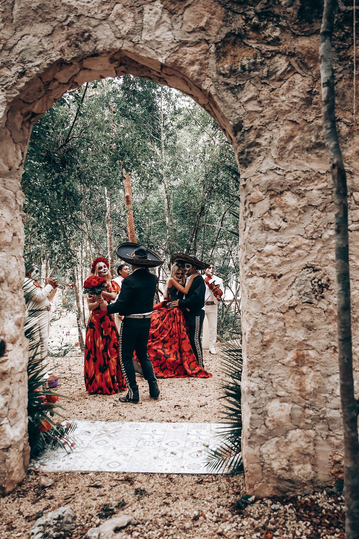 Stone archway frames a scene with figures in red and black clothing against a wooded backdrop.