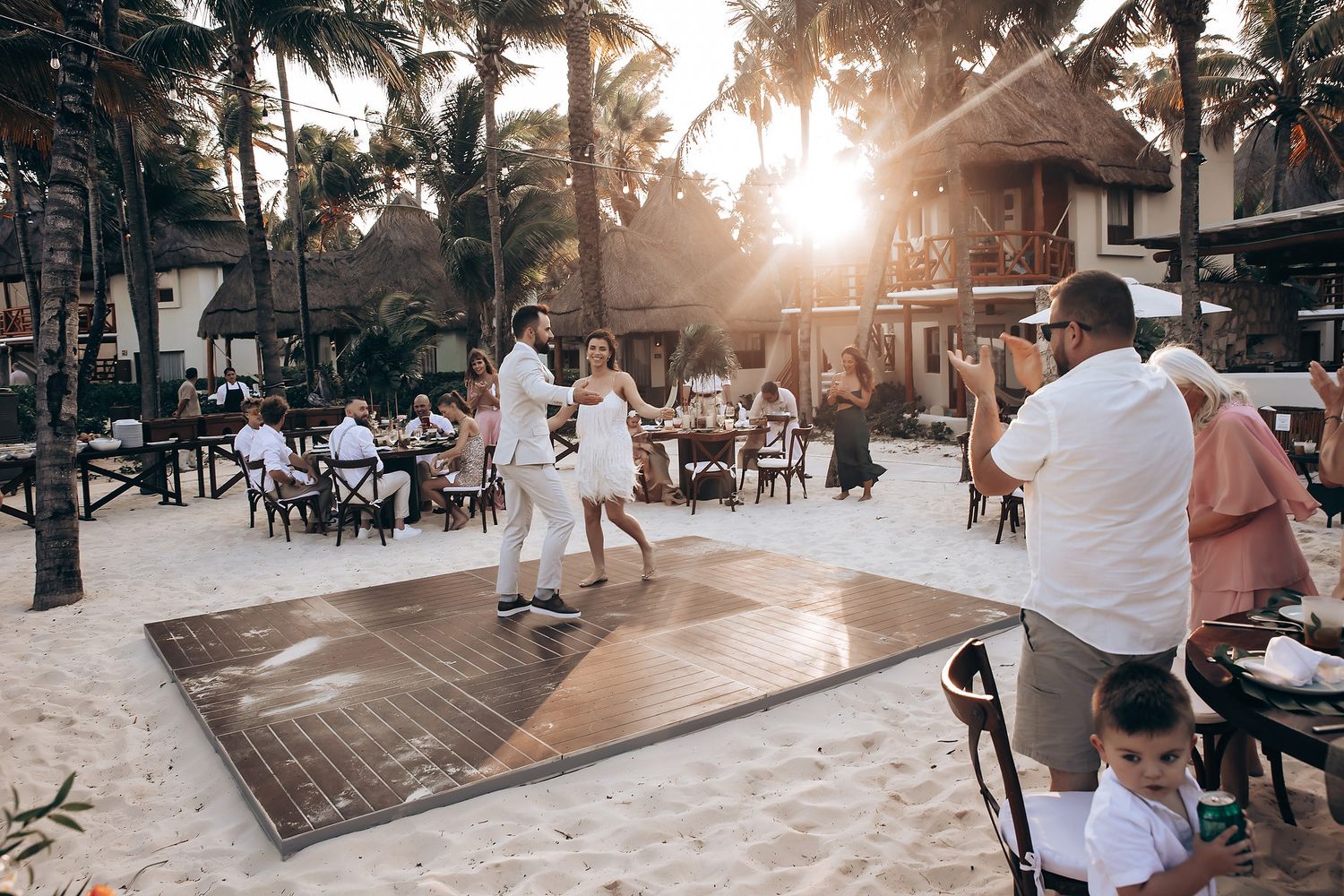 Sunset celebration at a beachside wedding reception with palm trees in the background.
