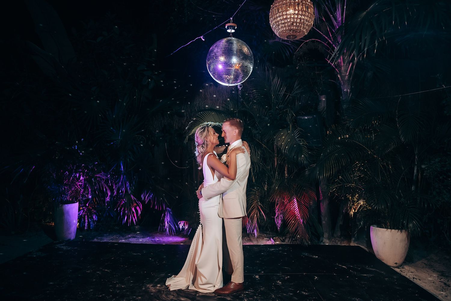 Couple shares an intimate moment under disco balls and purple lighting at their reception.