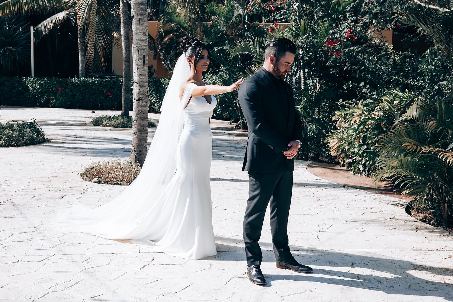 A couple participating in their first look wedding moment on a palm-lined pathway.