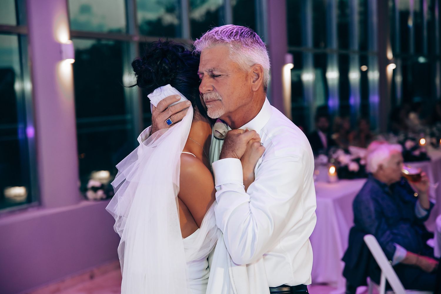 Wedding reception guests dancing and celebrating under purple mood lighting.