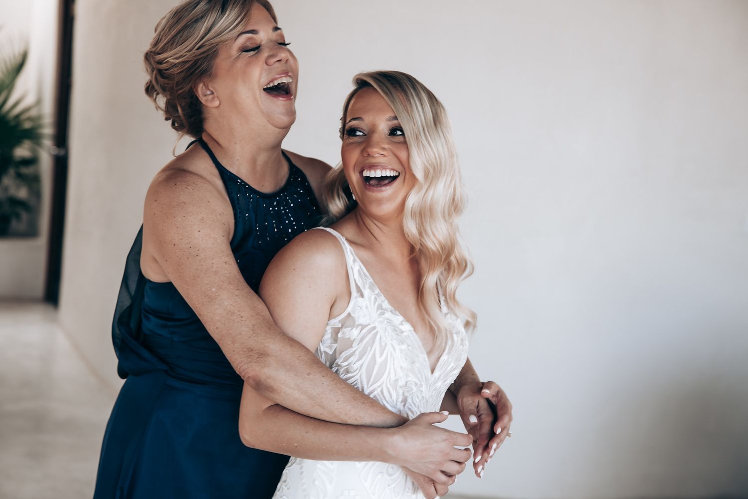 A couple shares joyful laughter together in a bright indoor setting while embracing in formal attire.