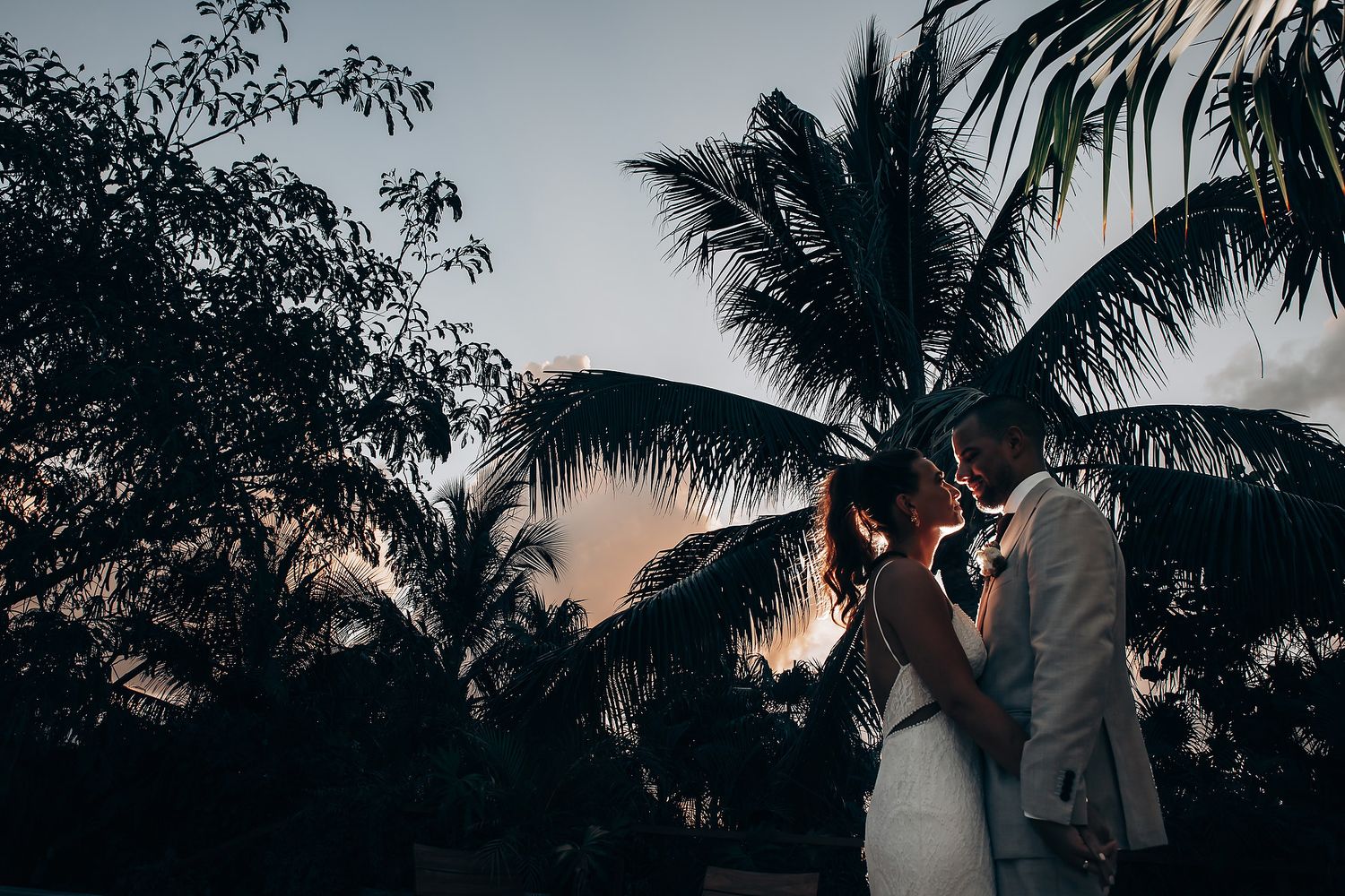 Silhouetted palm trees frame sunset wedding ceremony on tropical beach.