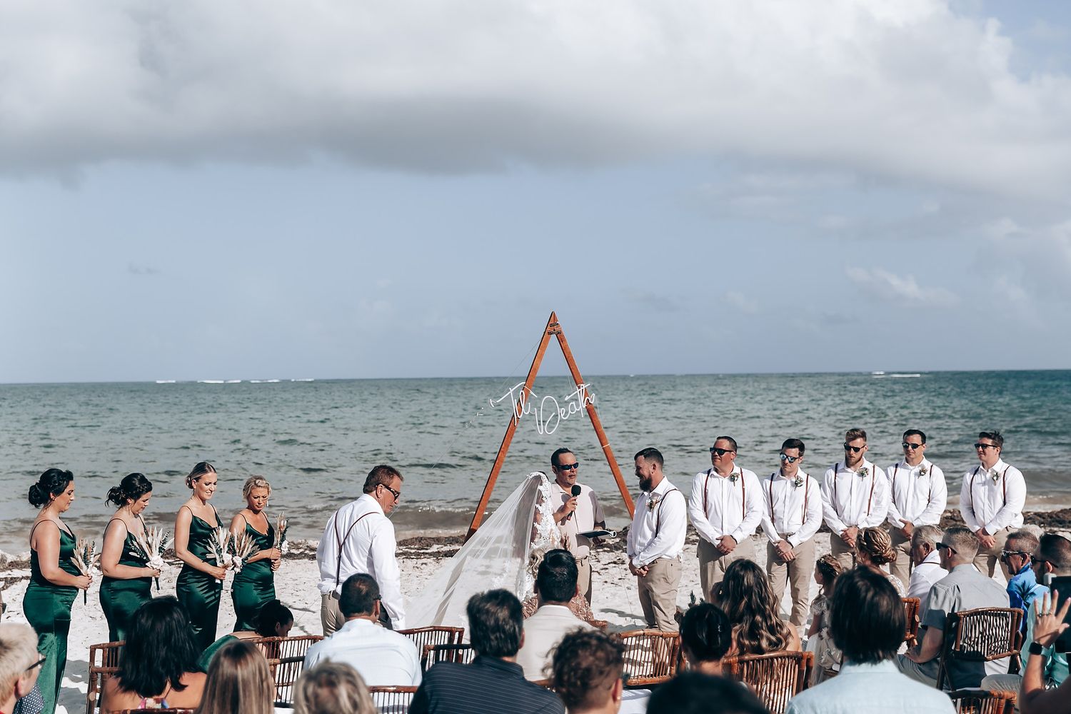 Beach wedding ceremony setup with guests seated under blue skies.