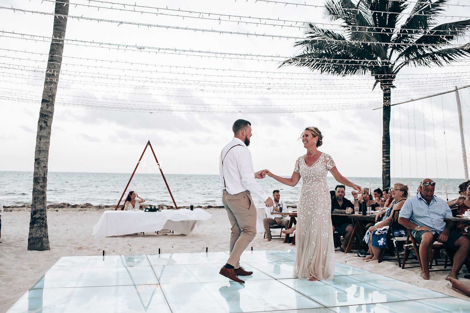 Palm trees and string lights decorate beachfront wedding venue at sunset.