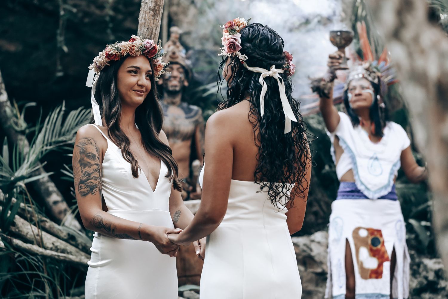 Wedding guests gather in a wooded area decorated with white fabric and floral elements for an outdoor celebration.