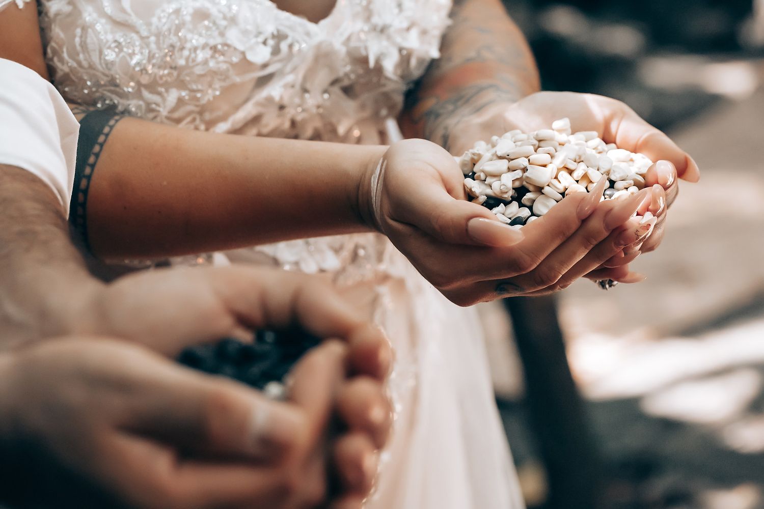Hands hold small ceremonial items during an outdoor wedding celebration.