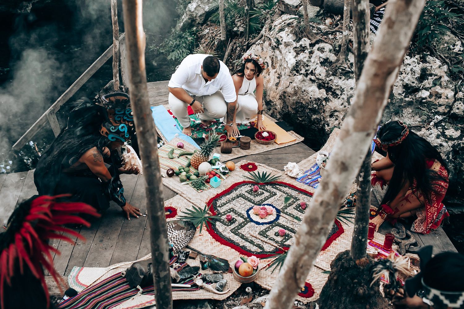 Spiritual ceremony with colorful tapestry and ritual objects laid out on ground in natural setting.