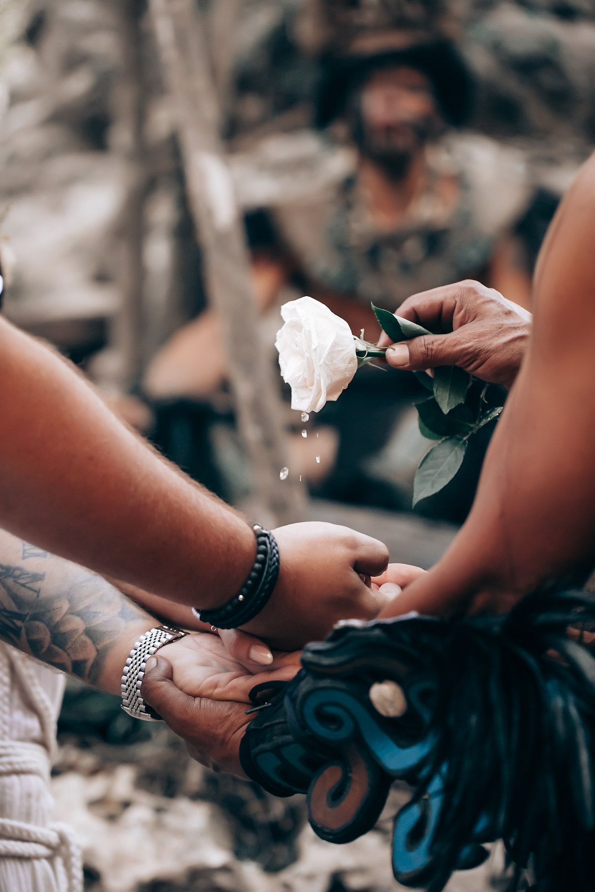 Close-up of hands exchanging white roses during an outdoor ceremony.