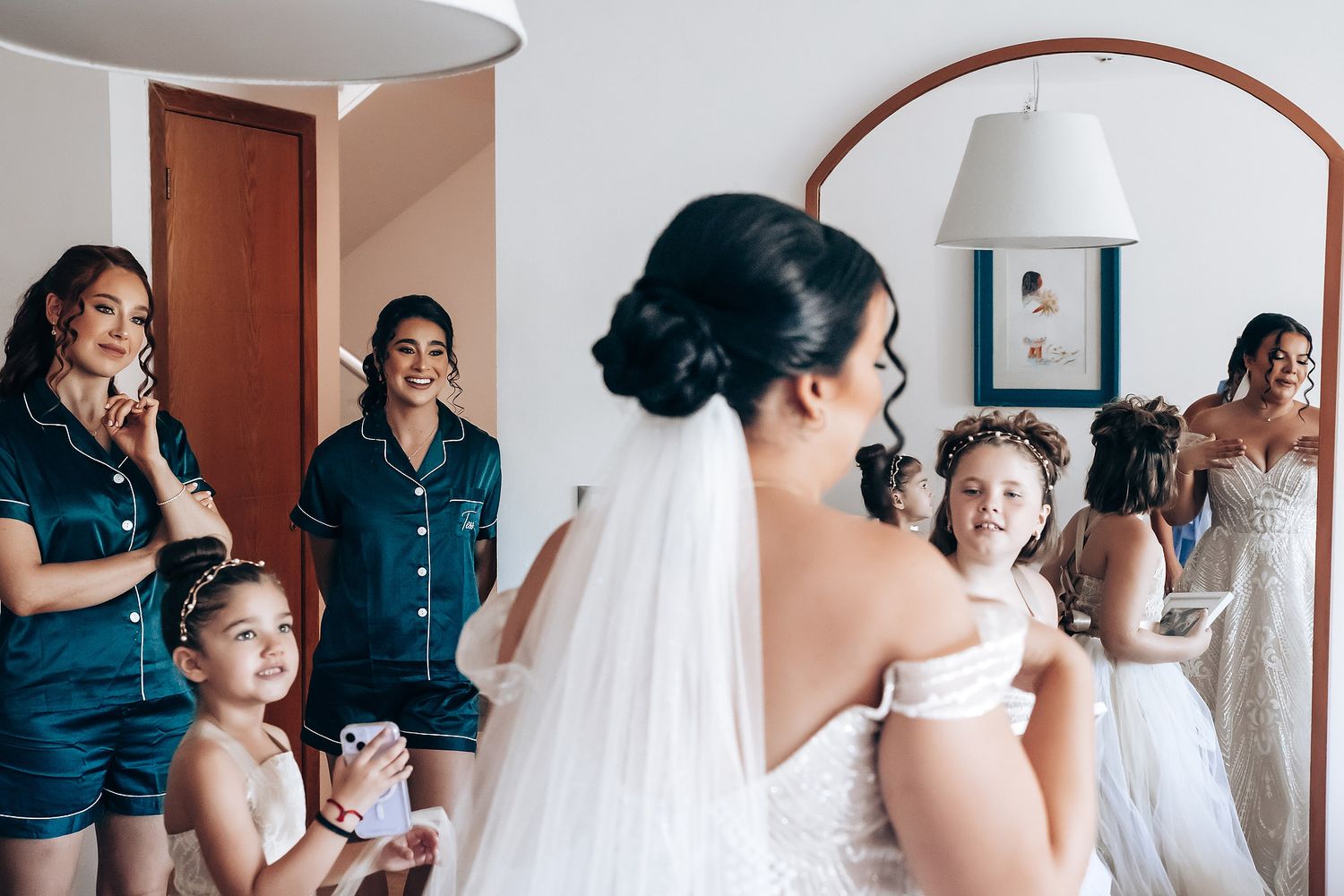 Wedding party getting ready in a bright room with white curtains and elegant attire.