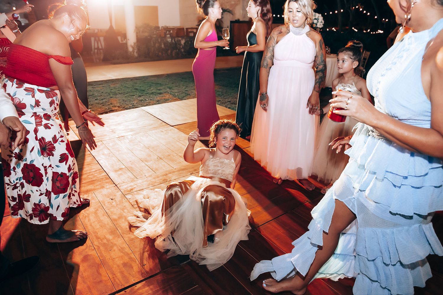 Wedding guests dancing and celebrating on a wooden dance floor at an evening reception.