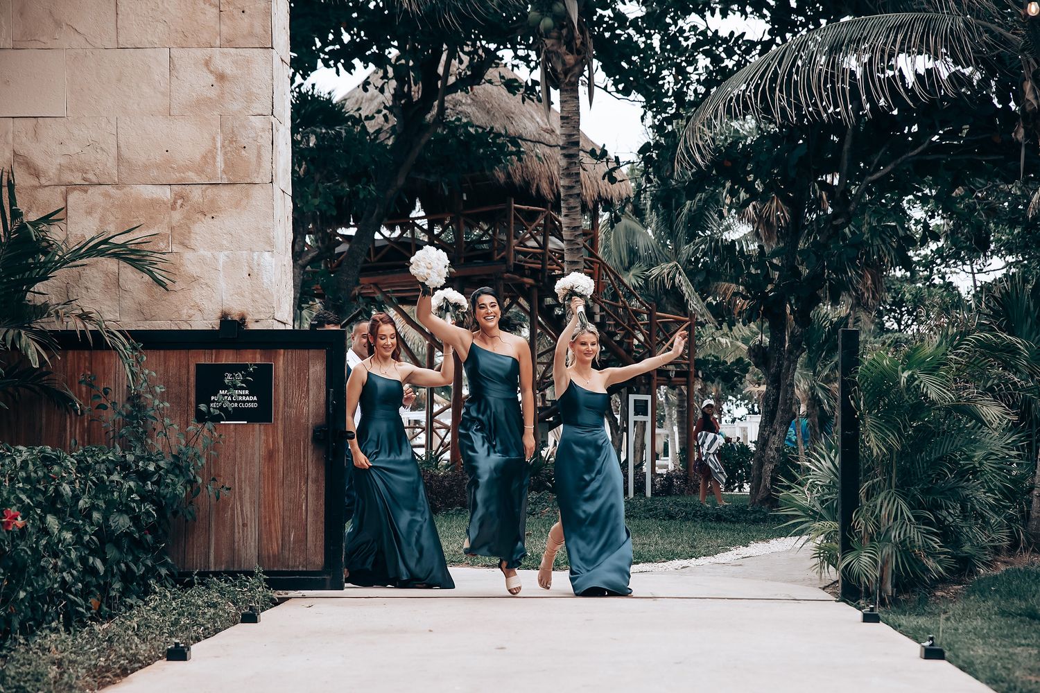 Wedding party in blue dresses poses together outdoors among tropical palm trees.