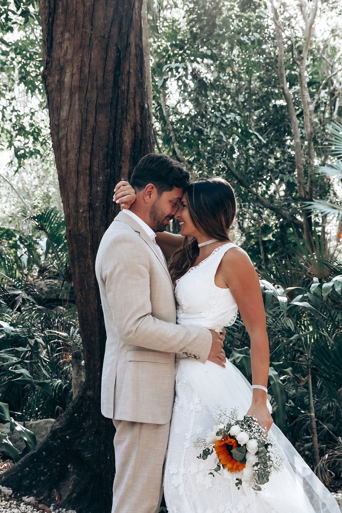 Romantic wedding moment captured among tall trees in a lush garden setting.
