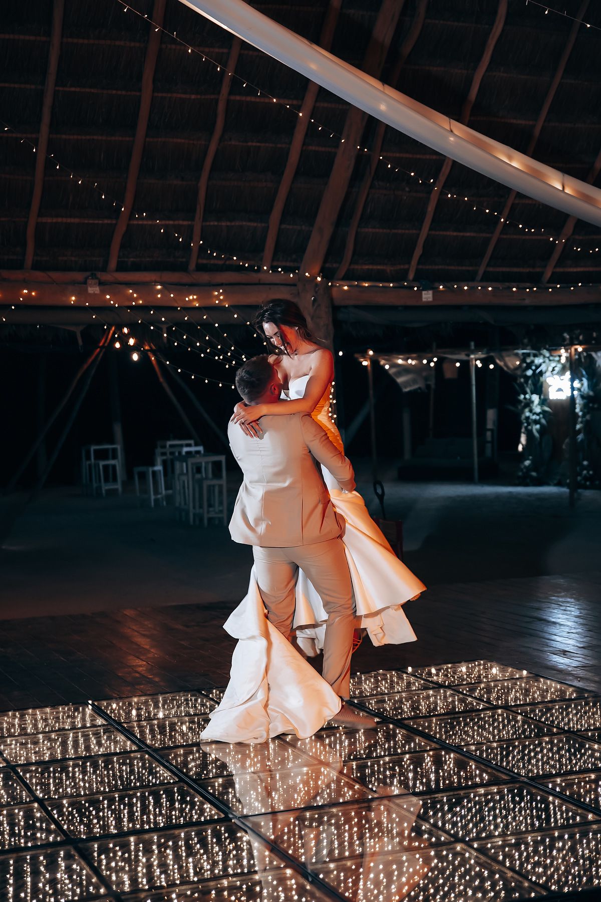 A couple dances intimately on a reflective floor at their wedding reception under twinkling lights.