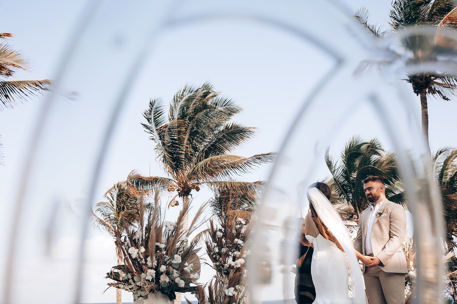 A couple shares a romantic moment under swaying palm trees on a tropical beach during sunset.