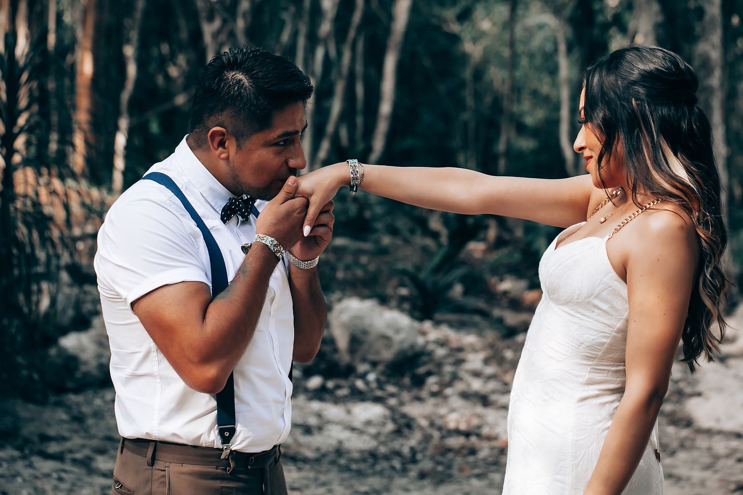 A couple in formal wedding attire shares romantic moments in a wooded outdoor setting during their special day.