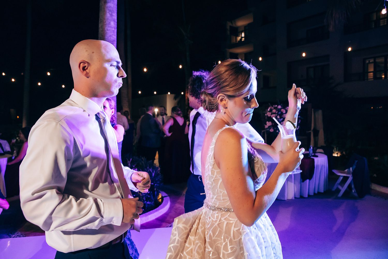 A bride and groom dancing together at their wedding reception under colorful lighting.