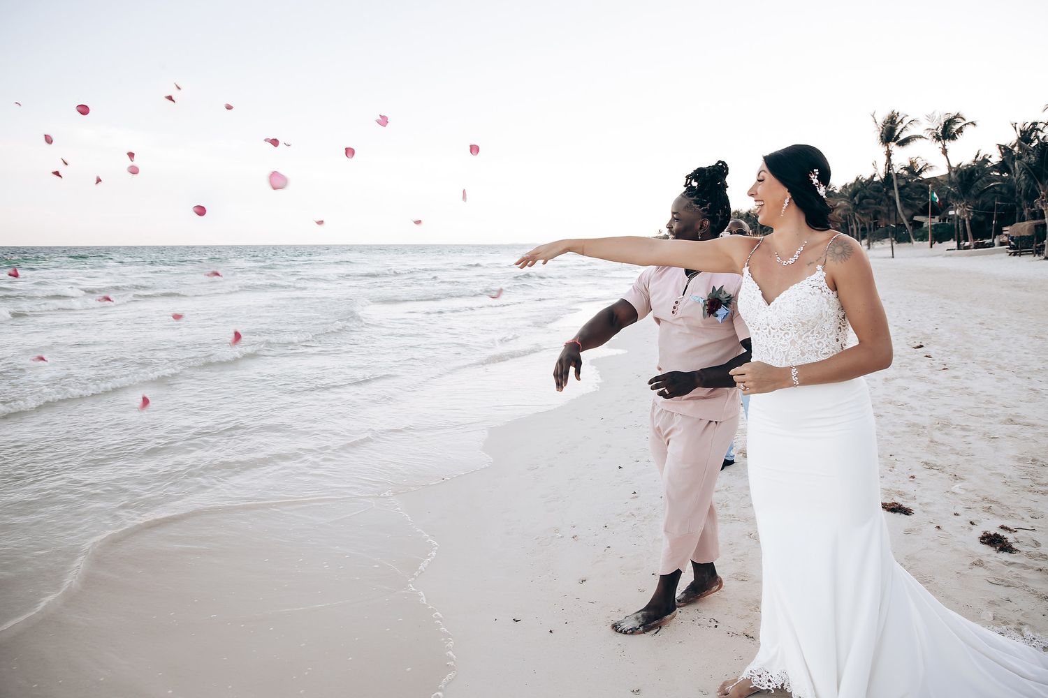 The image shows a bride and groom walking together on a beach, with rose petals falling around them.