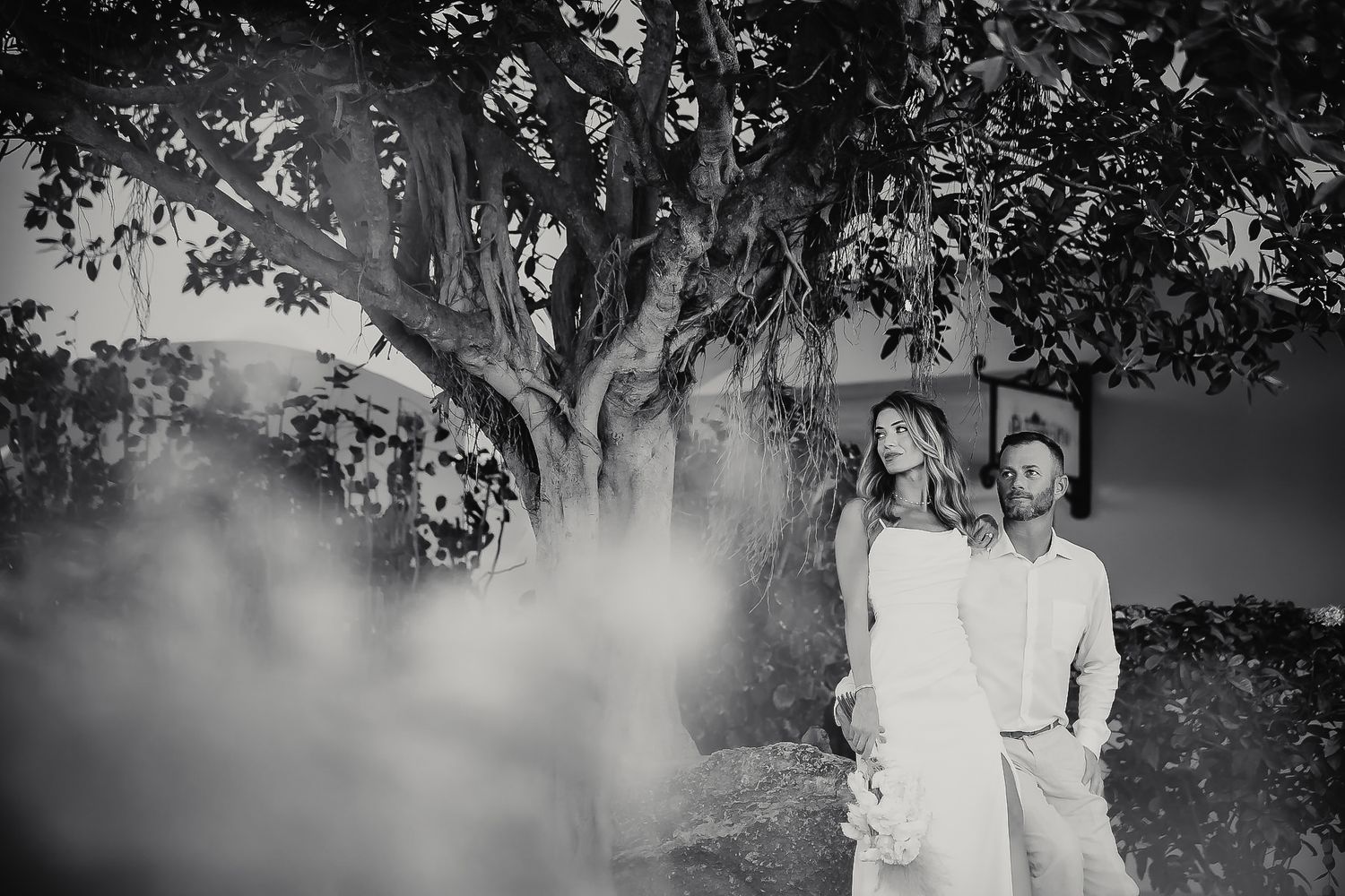 A black and white portrait of a couple embracing in a natural setting.