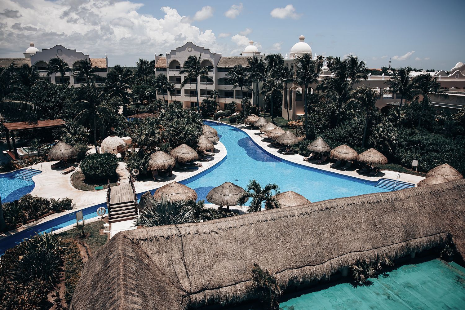 An image showing a large resort with multiple buildings, pools, and palm trees in a tropical setting.
