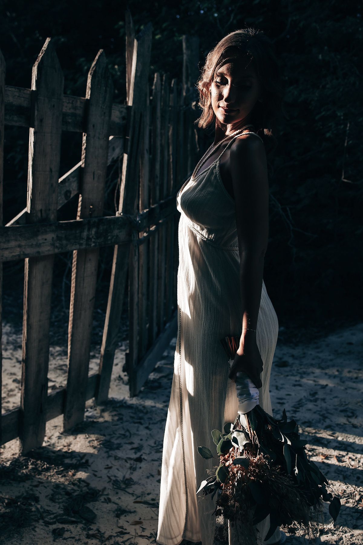 A woman in a white dress stands in a dimly lit, rustic setting.