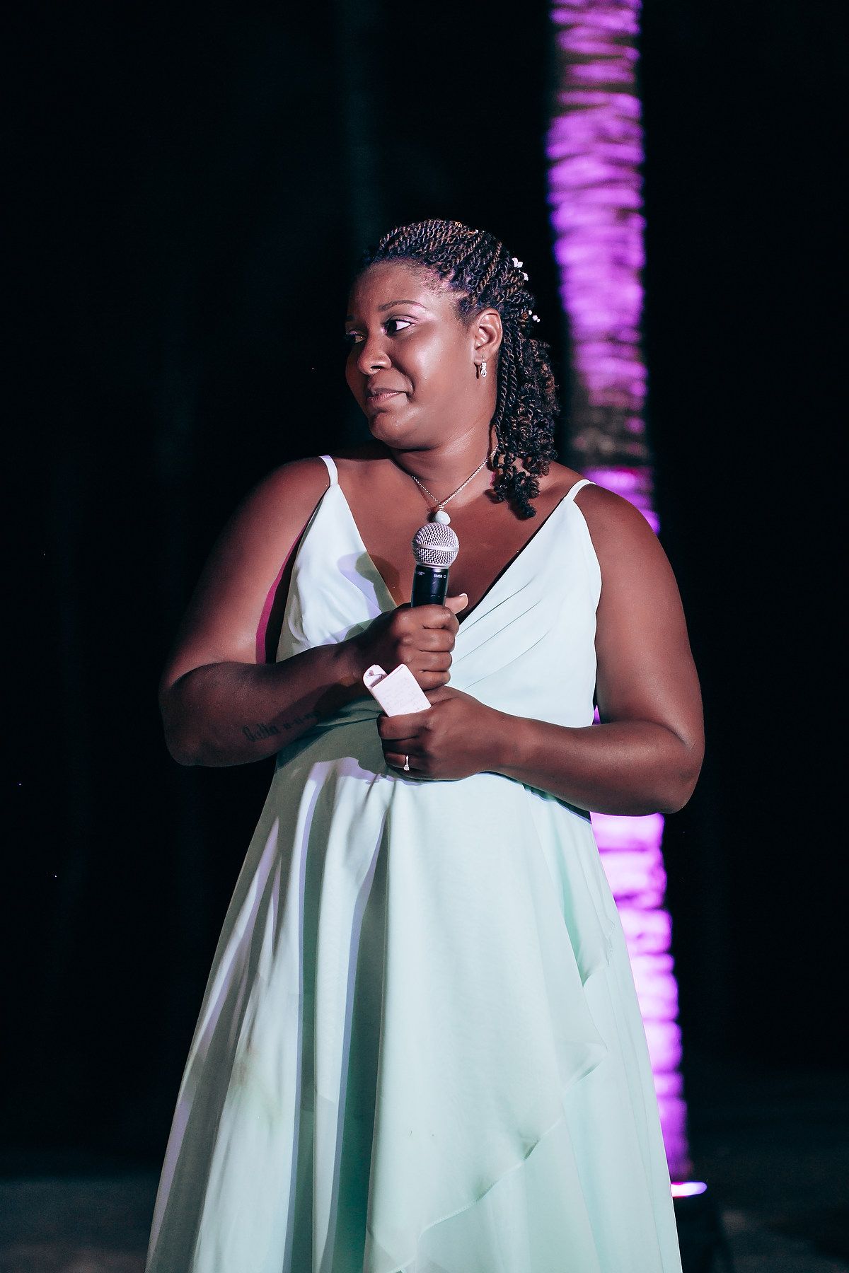 A person in a white dress holding a microphone during an evening event with purple lighting.