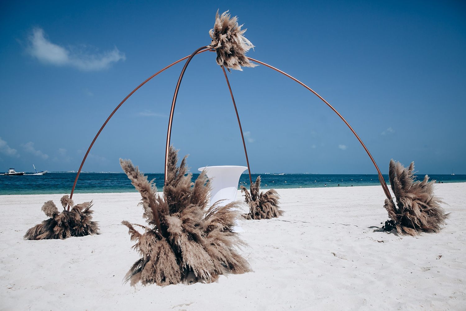 Dried palm fronds arching over pristine white sand beach against bright blue sky.
