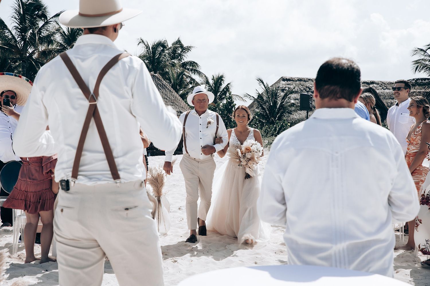 A beachside wedding ceremony with guests dressed in light summer attire and suspenders.