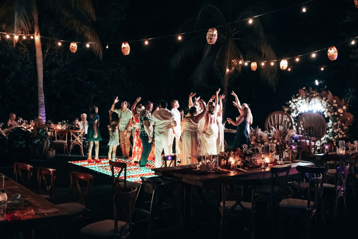 Wedding guests dancing under string lights at a vibrant outdoor tropical evening reception.