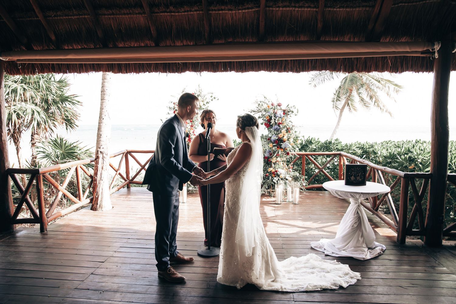 Bride and groom standing with officiant during their intimate tropical beachside wedding ceremony under a palapa.
