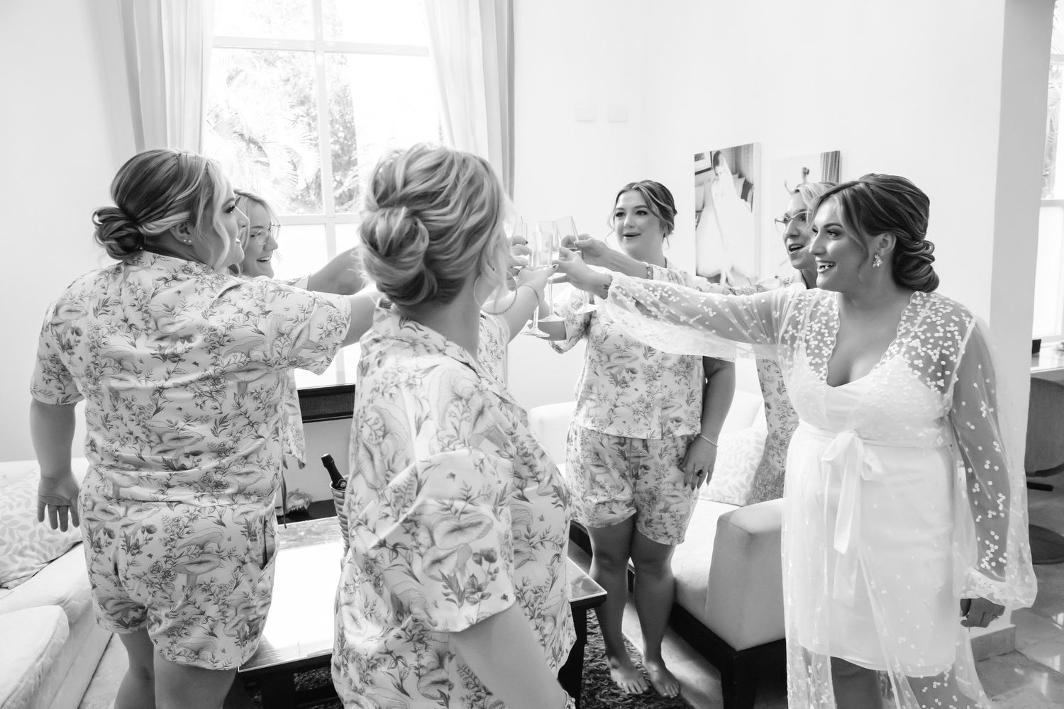 Bridesmaids in floral robes helping bride prepare on wedding morning in black and white.
