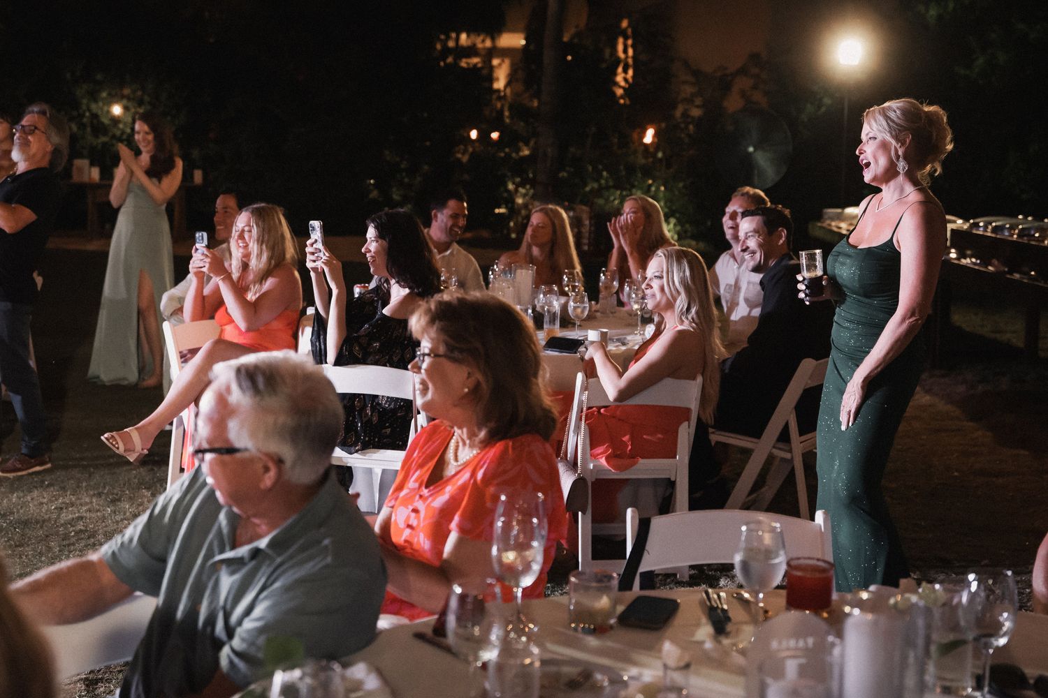Wedding guests celebrate and photograph at elegantly decorated outdoor nighttime reception with string lights.