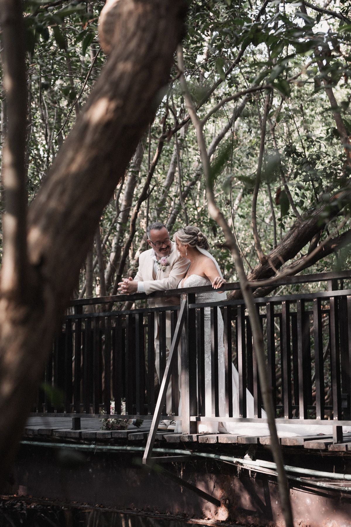 Bride and groom sharing romantic moment on wooden bridge surrounded by mangrove trees.