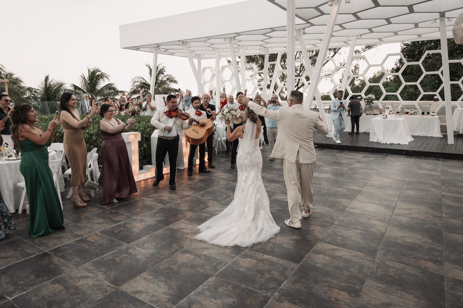 Bride and groom share first dance on rooftop venue while mariachi band serenades wedding guests.