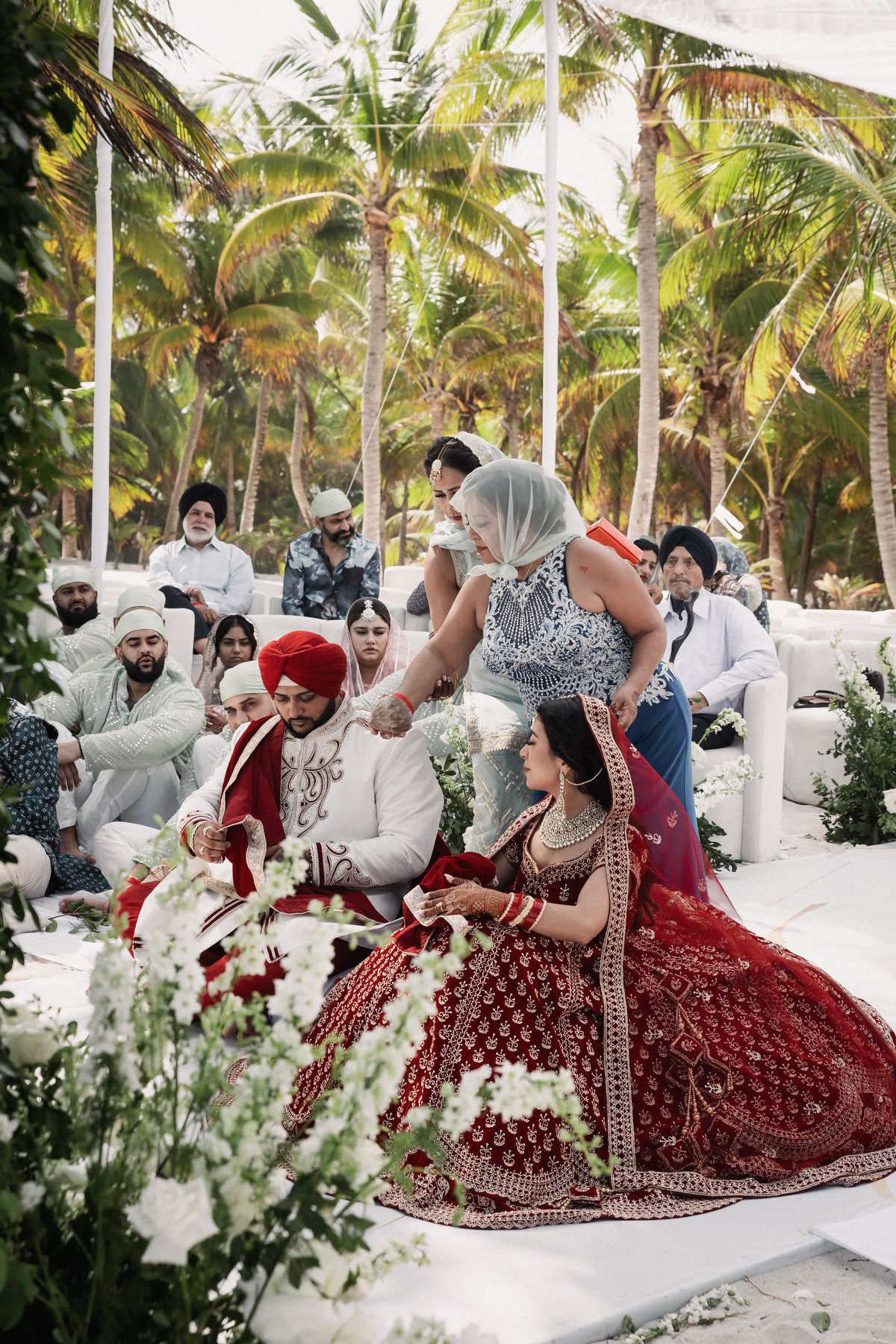 Indian wedding ceremony with bride and groom in red and white attire at tropical outdoor mandap.
