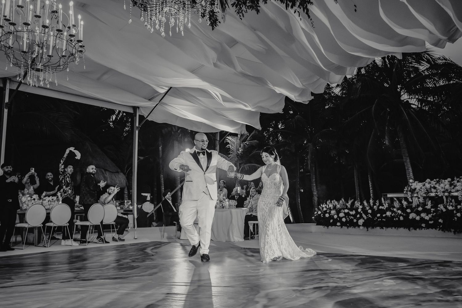 Black and white photo of bride and groom sharing first dance under draped tent at outdoor wedding reception.