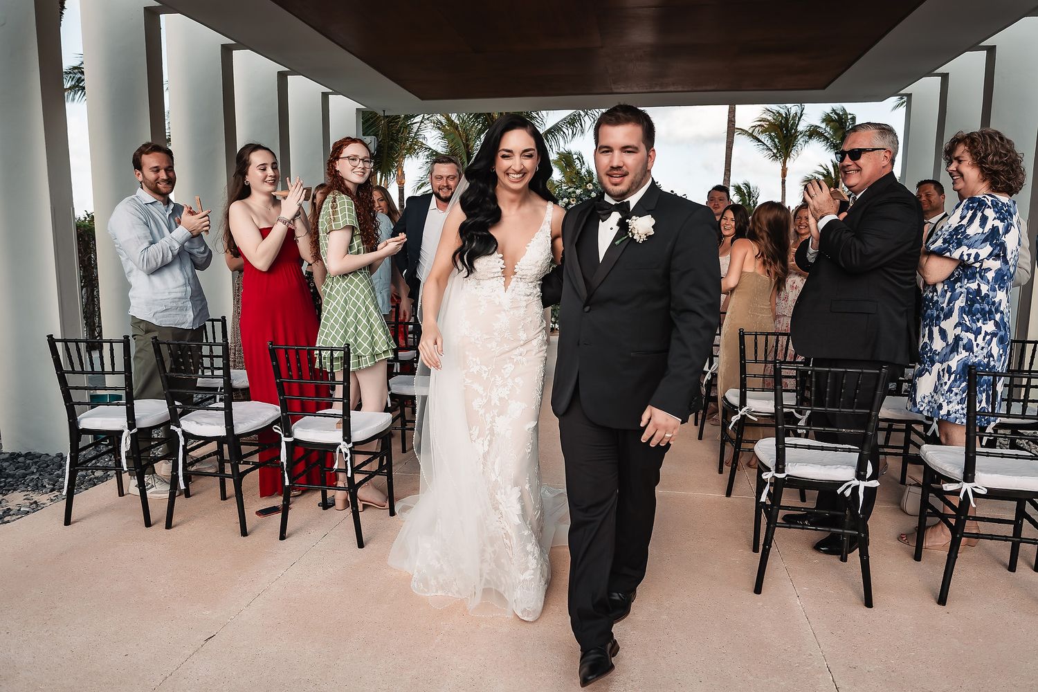 Bride and groom walk down the aisle as guests applaud at an outdoor wedding ceremony.