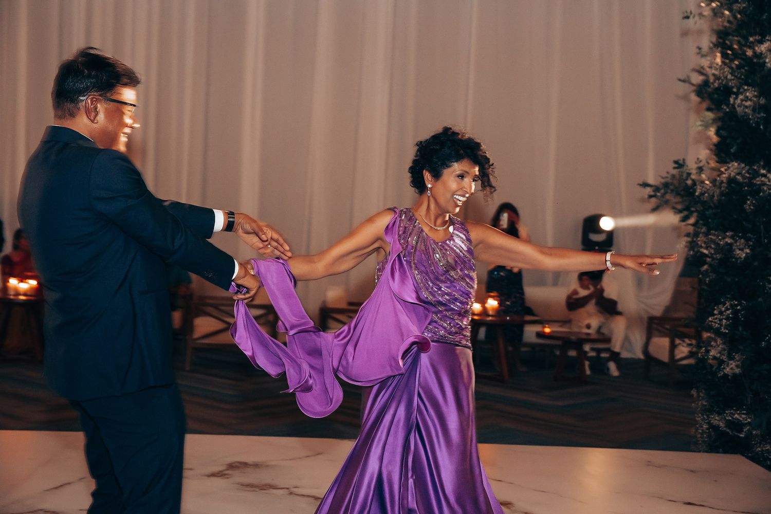 Couple dancing energetically on a ballroom floor, with the person in a flowing purple dress spinning.