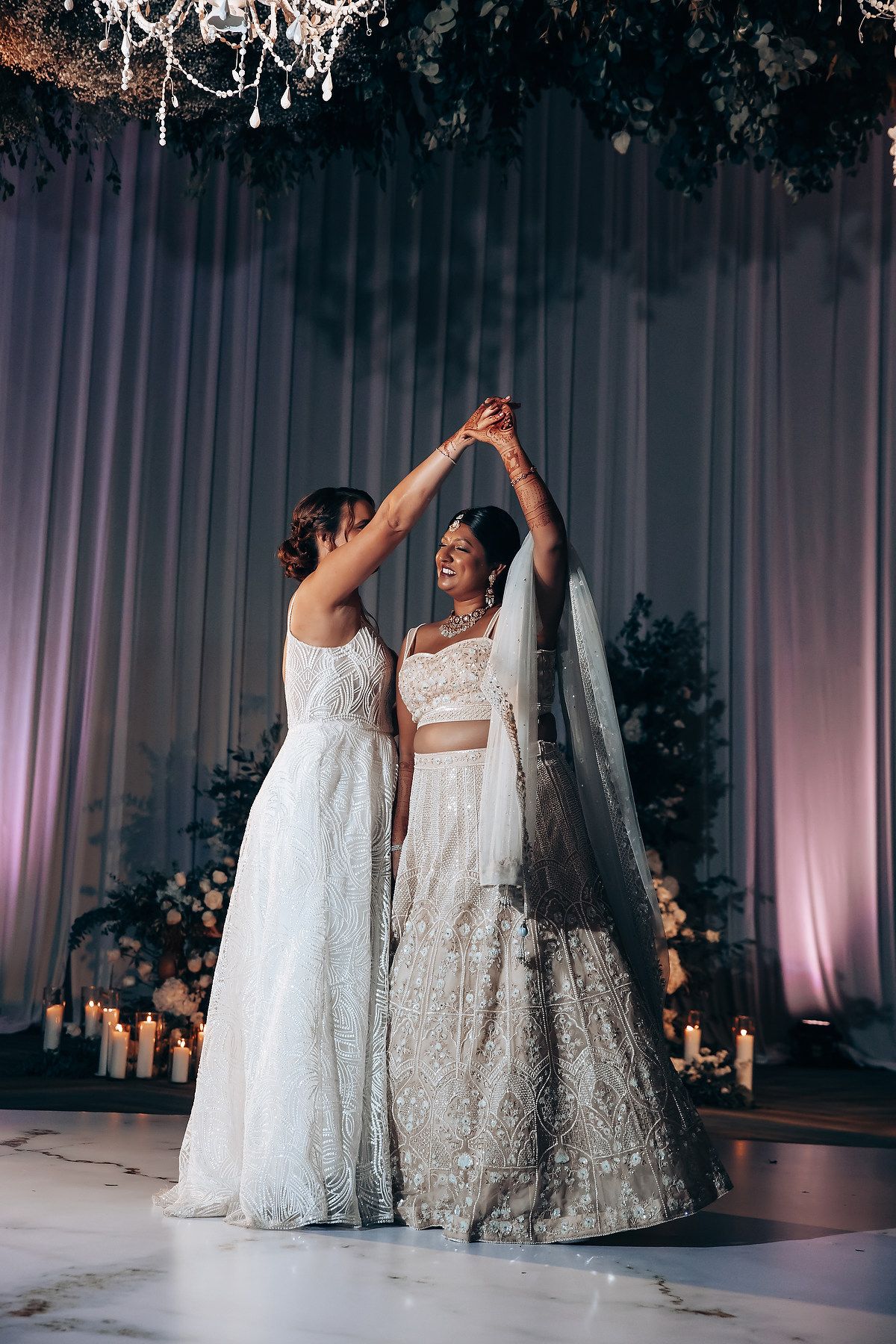 Two people in elegant white wedding dresses dance together in a beautifully decorated reception hall.
